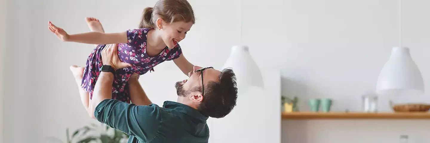 Mann hebt Kind mit den Armen ueber seinen Koerper