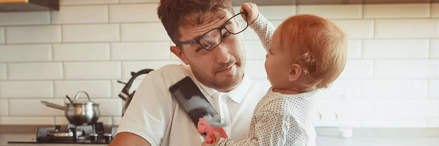 Vater mit Kind auf dem Arm, das an der Brille des Vaters zieht.