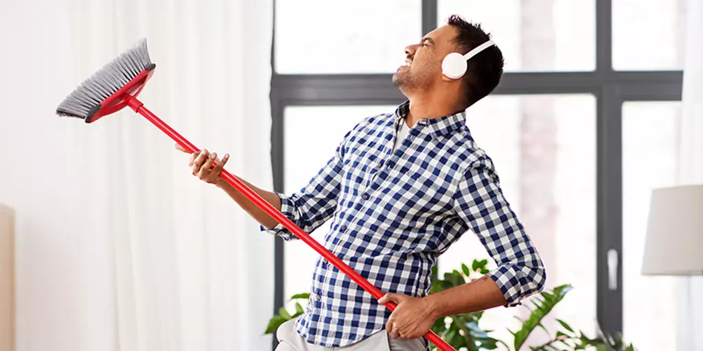 Mann mit Kopfhörern hält einen Besen wie eine Gitarre 