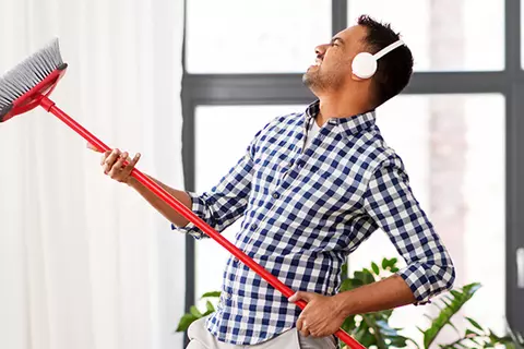 Mann mit Kopfhörern hält einen Besen wie eine Gitarre 