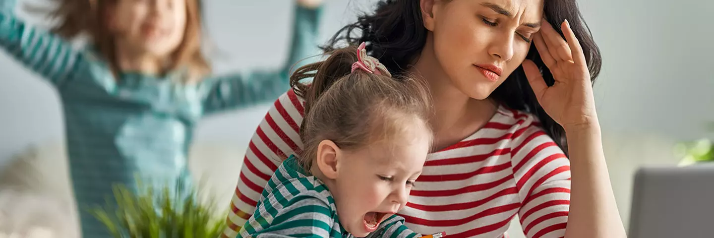 Gestresste Mutter am Laptop mit tobenden Kindern