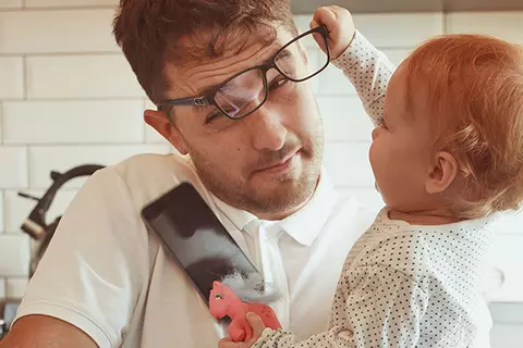 Vater mit Kind auf dem Arm, das an der Brille des Vaters zieht.